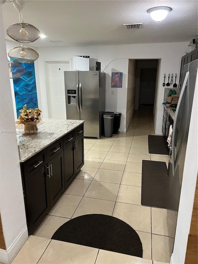 kitchen with stainless steel refrigerator with ice dispenser, light stone countertops, a textured ceiling, and light tile patterned floors