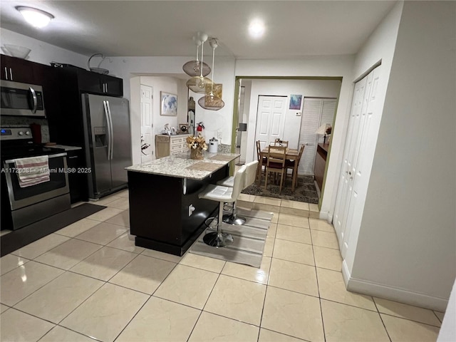 kitchen with stainless steel appliances, light tile patterned floors, light stone counters, and a kitchen breakfast bar