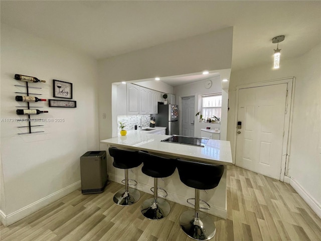 kitchen featuring stainless steel refrigerator, sink, white cabinets, a kitchen breakfast bar, and kitchen peninsula