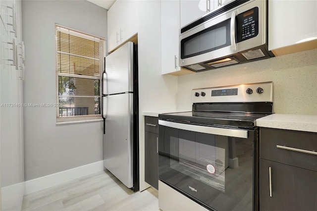 kitchen with stainless steel appliances, dark brown cabinetry, white cabinets, decorative backsplash, and light wood-type flooring