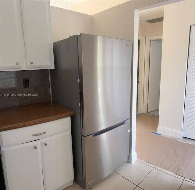 kitchen featuring stainless steel refrigerator, light tile patterned flooring, decorative backsplash, and white cabinets