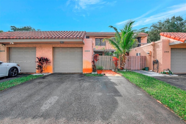 view of front of home with stucco siding, aphalt driveway, fence, a garage, and a tiled roof