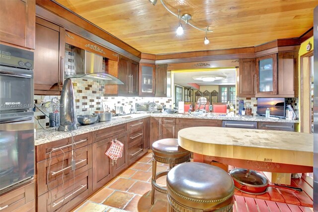 kitchen with light stone counters, double wall oven, backsplash, and wooden ceiling