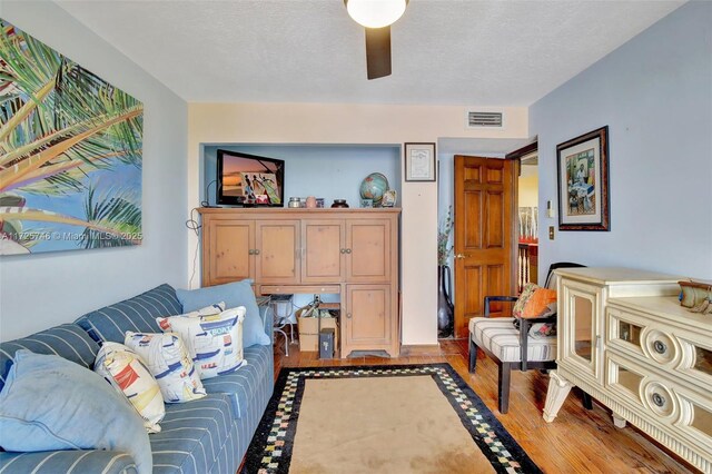 living room featuring ceiling fan, wood-type flooring, and a textured ceiling