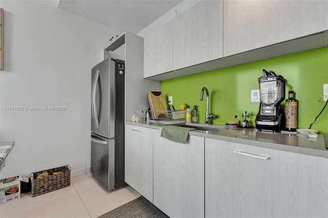 kitchen featuring white cabinetry, sink, light tile patterned floors, and stainless steel refrigerator