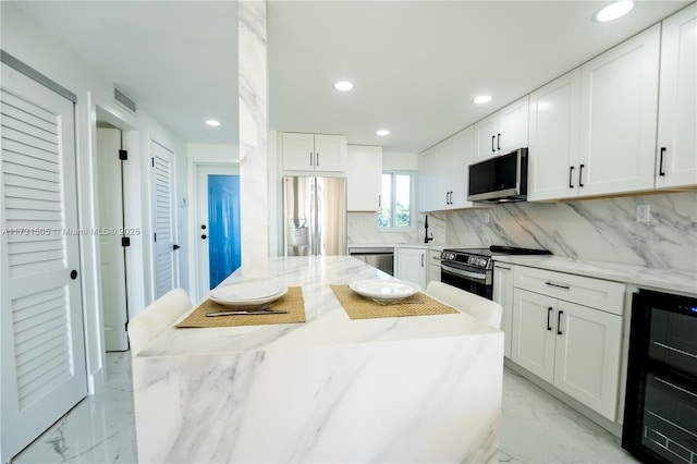 kitchen with appliances with stainless steel finishes, white cabinetry, wine cooler, decorative backsplash, and light stone countertops