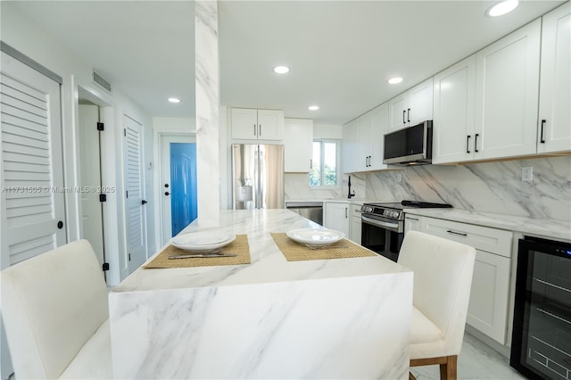 kitchen with white cabinetry, appliances with stainless steel finishes, beverage cooler, and tasteful backsplash