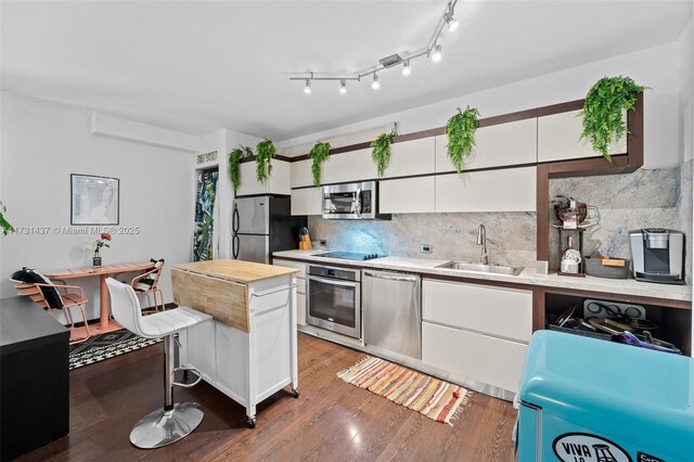 kitchen with sink, white cabinetry, dark hardwood / wood-style floors, stainless steel appliances, and decorative backsplash