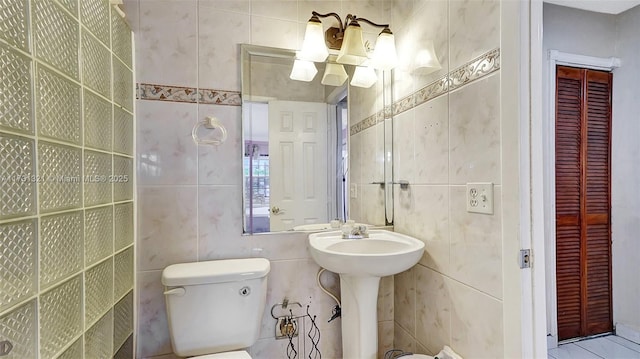 bathroom with toilet, sink, and tile walls