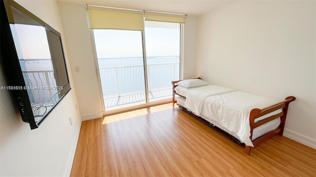 bedroom featuring expansive windows, a water view, access to exterior, and light wood-type flooring