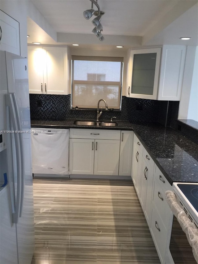 kitchen featuring sink, white appliances, white cabinetry, backsplash, and dark stone counters