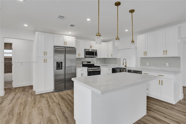 kitchen featuring light hardwood / wood-style flooring, appliances with stainless steel finishes, white cabinetry, a center island, and decorative light fixtures