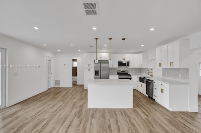 kitchen featuring a kitchen island, appliances with stainless steel finishes, pendant lighting, white cabinetry, and light hardwood / wood-style floors