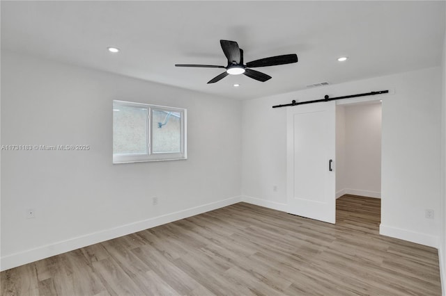 empty room featuring ceiling fan, a barn door, and light hardwood / wood-style flooring