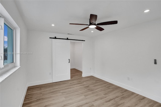 unfurnished bedroom with ceiling fan, a barn door, and light hardwood / wood-style floors