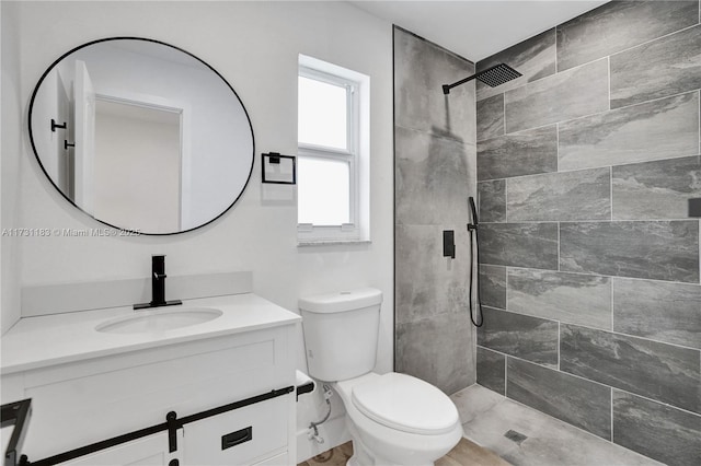 bathroom featuring a tile shower, vanity, and toilet