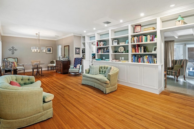 living area with built in shelves, ornamental molding, light hardwood / wood-style floors, and a notable chandelier