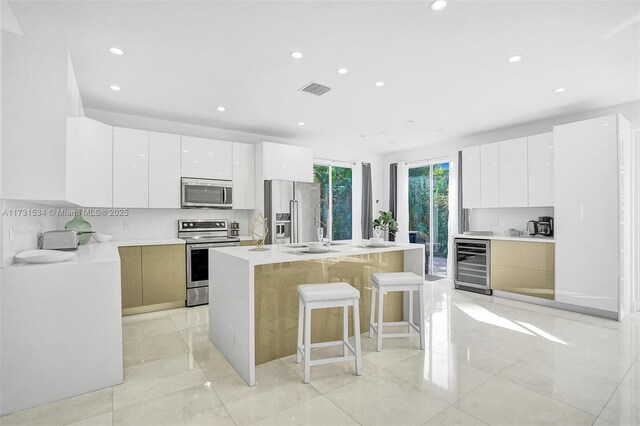 kitchen with a breakfast bar, white cabinetry, stainless steel appliances, wine cooler, and a center island with sink