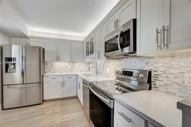 kitchen featuring sink, appliances with stainless steel finishes, backsplash, light stone counters, and white cabinets