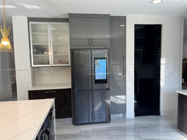 kitchen with tasteful backsplash, light stone countertops, stainless steel refrigerator, and dark brown cabinetry