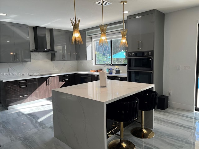 kitchen featuring decorative light fixtures, a kitchen bar, a center island, light stone counters, and wall chimney exhaust hood