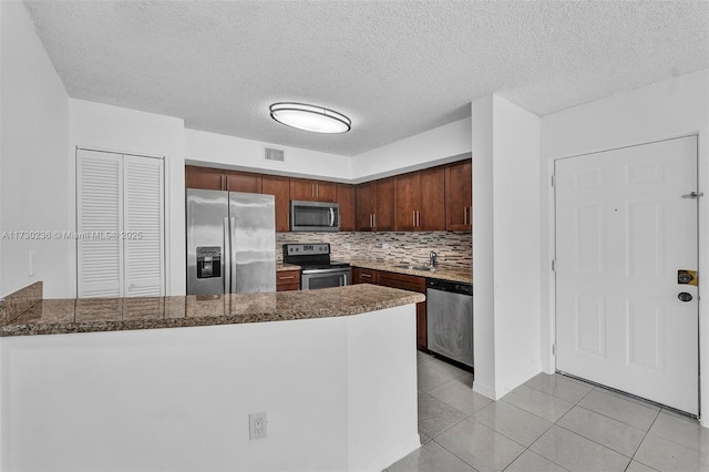 kitchen featuring a textured ceiling, light tile patterned floors, appliances with stainless steel finishes, kitchen peninsula, and decorative backsplash