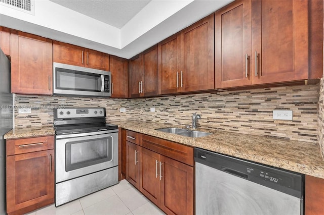 kitchen featuring tasteful backsplash, light stone countertops, appliances with stainless steel finishes, and sink