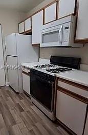 kitchen with white cabinetry, hardwood / wood-style floors, and white appliances