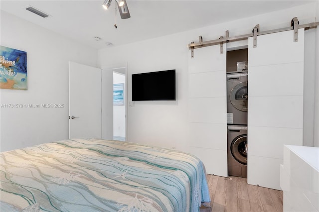 bedroom featuring ceiling fan, stacked washer and clothes dryer, a barn door, and a closet