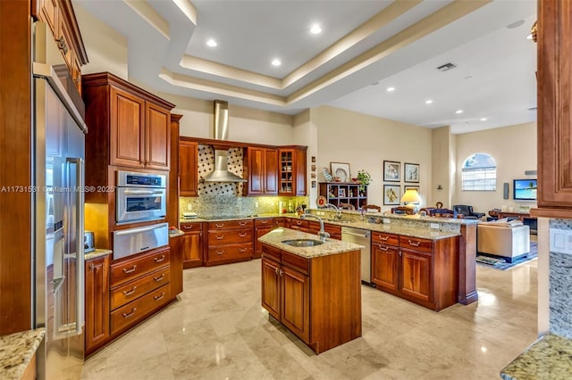 kitchen with sink, backsplash, stainless steel appliances, light stone counters, and a center island with sink