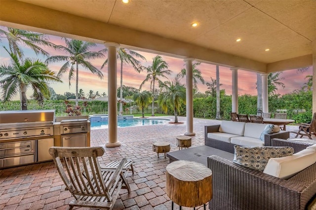 patio terrace at dusk featuring an outdoor kitchen, grilling area, and an outdoor hangout area