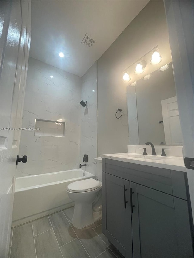 full bathroom featuring tiled shower / bath, vanity, and toilet