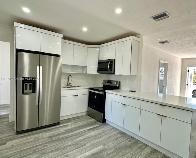 kitchen with sink, stainless steel appliances, a textured ceiling, white cabinets, and light wood-type flooring