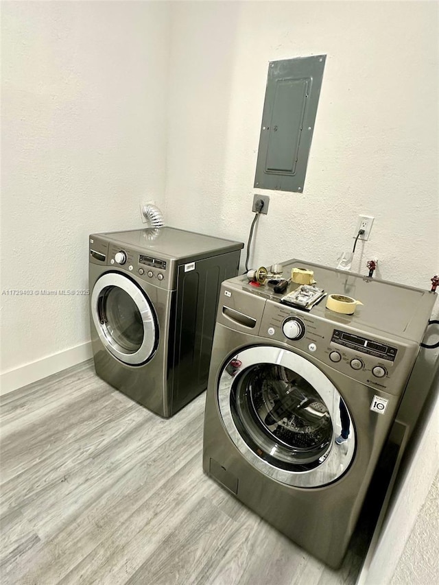 laundry area with washing machine and clothes dryer, electric panel, and light hardwood / wood-style flooring