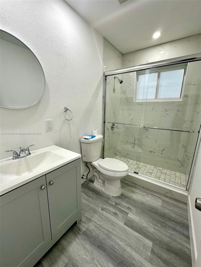 bathroom with vanity, a shower with shower door, wood-type flooring, and toilet