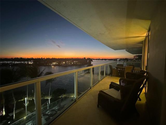 balcony at dusk featuring a water view