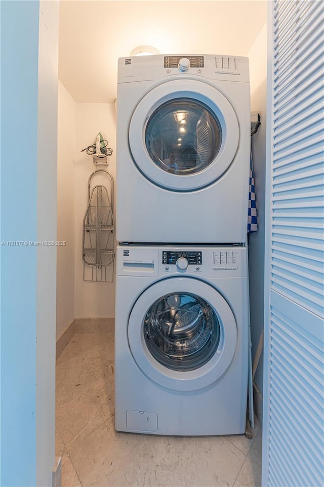 clothes washing area featuring stacked washer / drying machine and baseboards