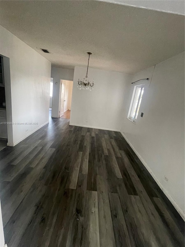 spare room with dark wood-type flooring, an inviting chandelier, and a textured ceiling