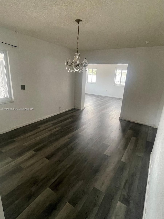 unfurnished dining area with an inviting chandelier, dark hardwood / wood-style floors, and a textured ceiling