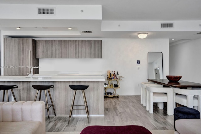 kitchen featuring sink, light wood-type flooring, kitchen peninsula, and a kitchen bar