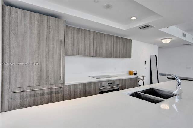 kitchen with black electric cooktop, sink, oven, and a raised ceiling