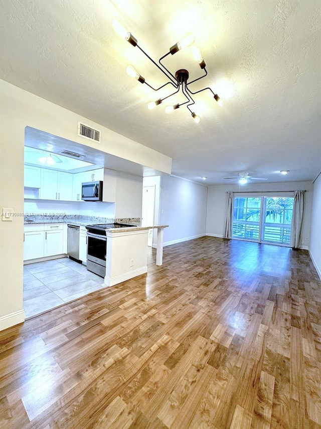 kitchen featuring appliances with stainless steel finishes, a textured ceiling, light hardwood / wood-style flooring, and white cabinets