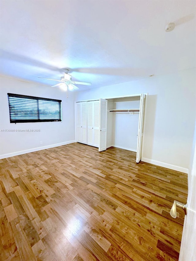 unfurnished bedroom featuring multiple closets, wood-type flooring, and ceiling fan