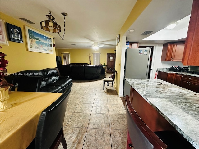 kitchen featuring reddish brown cabinets, light countertops, visible vents, freestanding refrigerator, and open floor plan