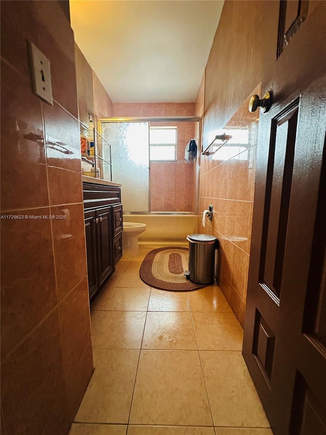 full bath featuring toilet, shower / bath combination with glass door, tile patterned flooring, vanity, and tile walls