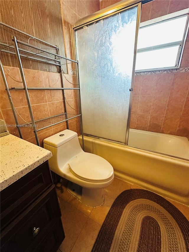 bathroom featuring toilet, shower / bath combination with glass door, tile patterned flooring, vanity, and tile walls