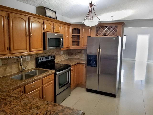 kitchen with sink, stainless steel appliances, decorative backsplash, light tile patterned flooring, and decorative light fixtures