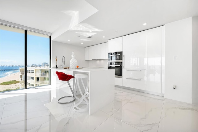 kitchen featuring white cabinetry, a water view, a kitchen breakfast bar, double oven, and expansive windows