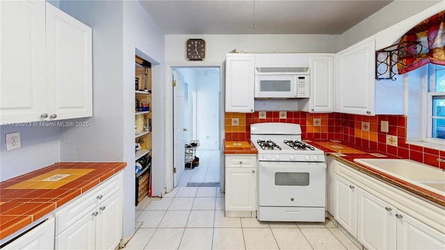 kitchen with light tile patterned flooring, tile countertops, white cabinetry, decorative backsplash, and white appliances