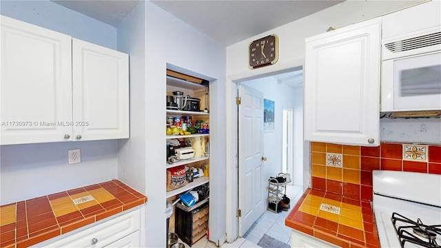 kitchen featuring light tile patterned flooring, stove, tile counters, and white cabinets